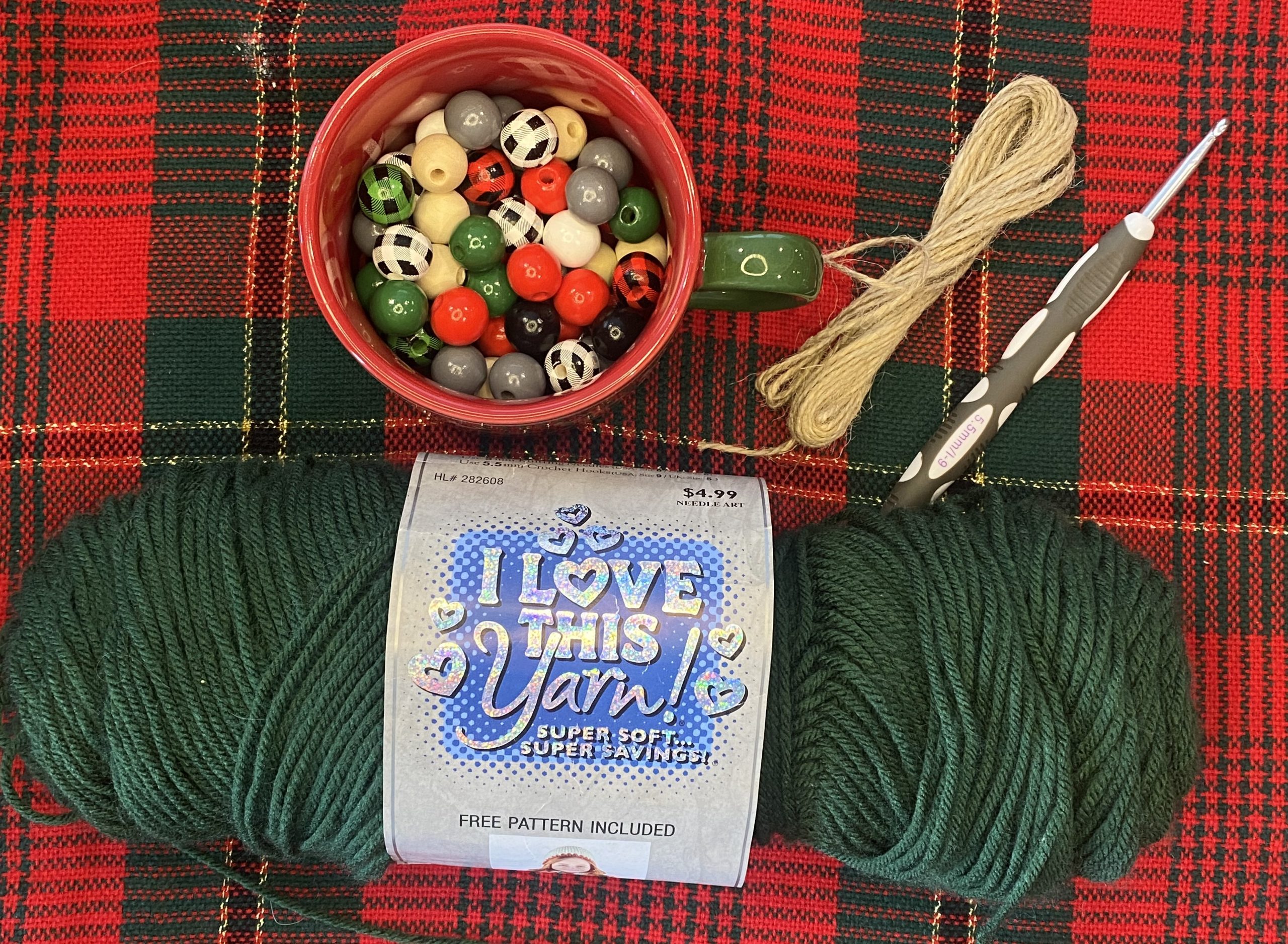 Wooden beads, twine, crochet hook, and green yarn on plaid background